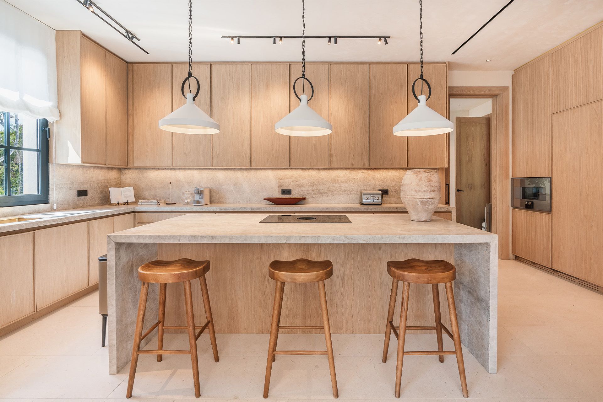Bright modern kitchen with wood cabinets, white island, three stools, and pendant lights