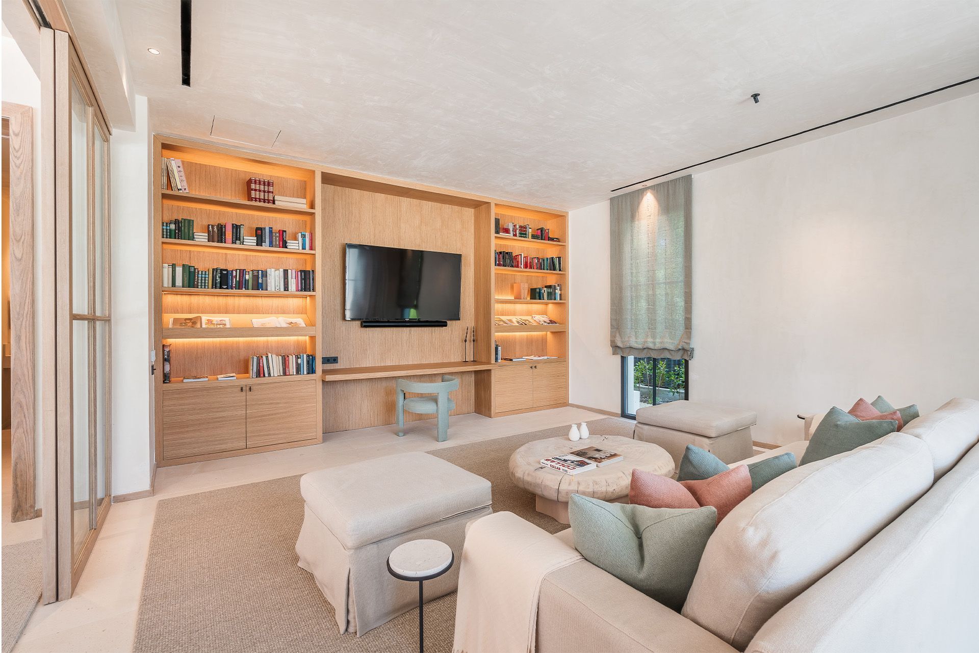 Bright living room with built-in wood shelves, wall-mounted TV, and a beige sectional sofa.