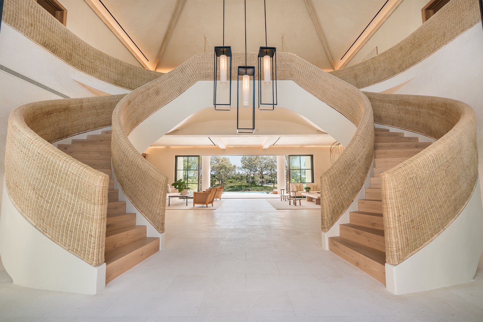 Modern interior with twin curved staircases, woven-texture walls, and hanging pendant lights under a high ceiling