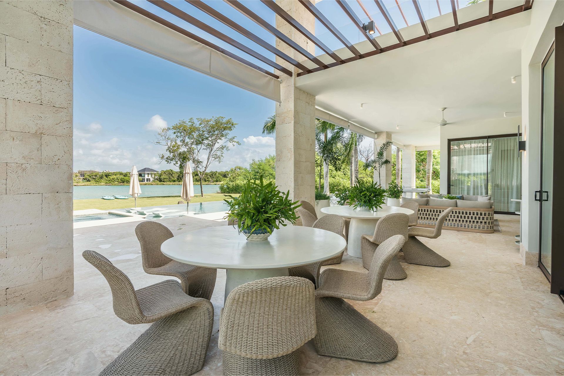 Covered patio with round table and woven chairs overlooking a pool and landscaped lawn. Mangle 15 