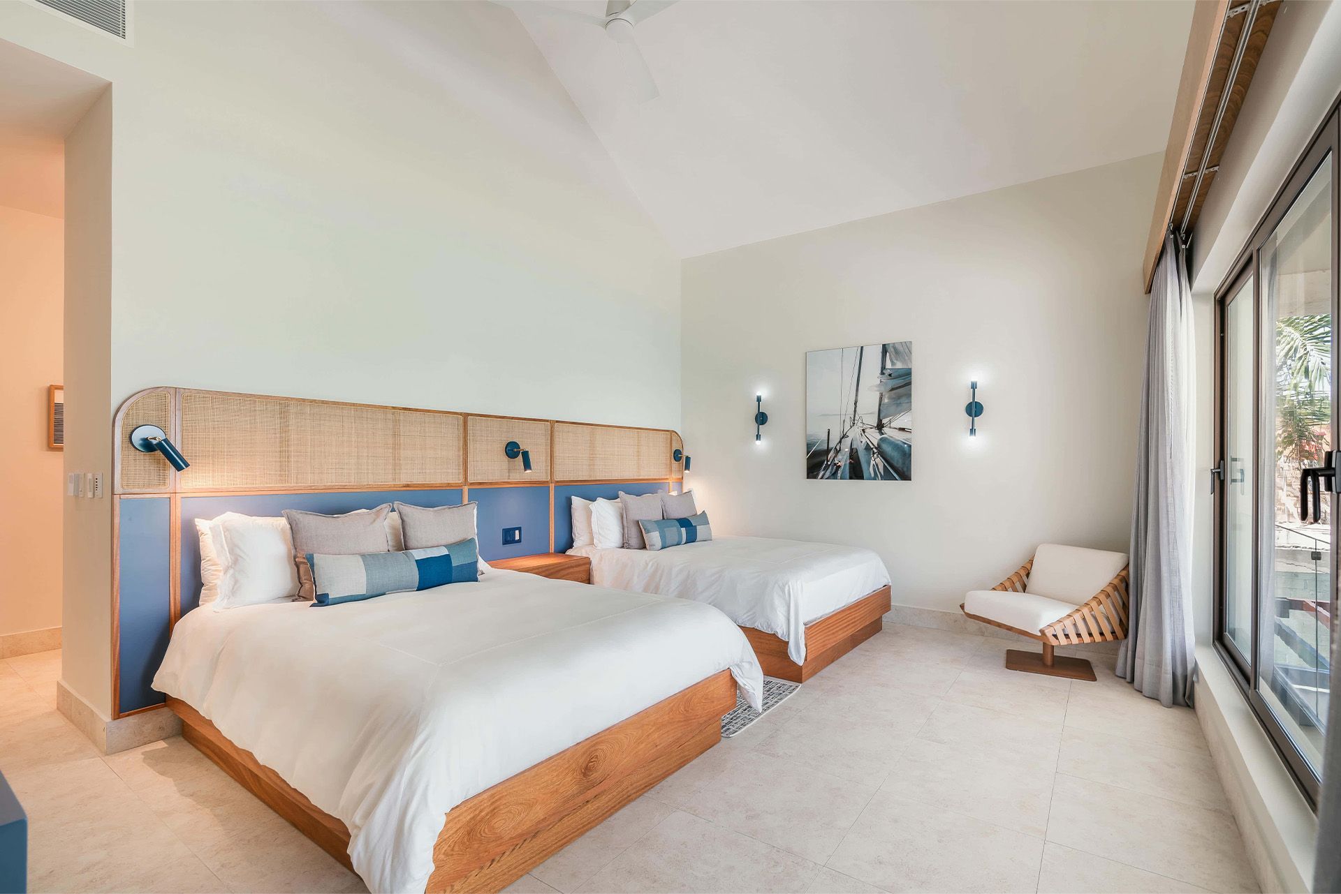 Spacious hotel bedroom with two beds, wall art, lounge chair, and large window overlooking the view