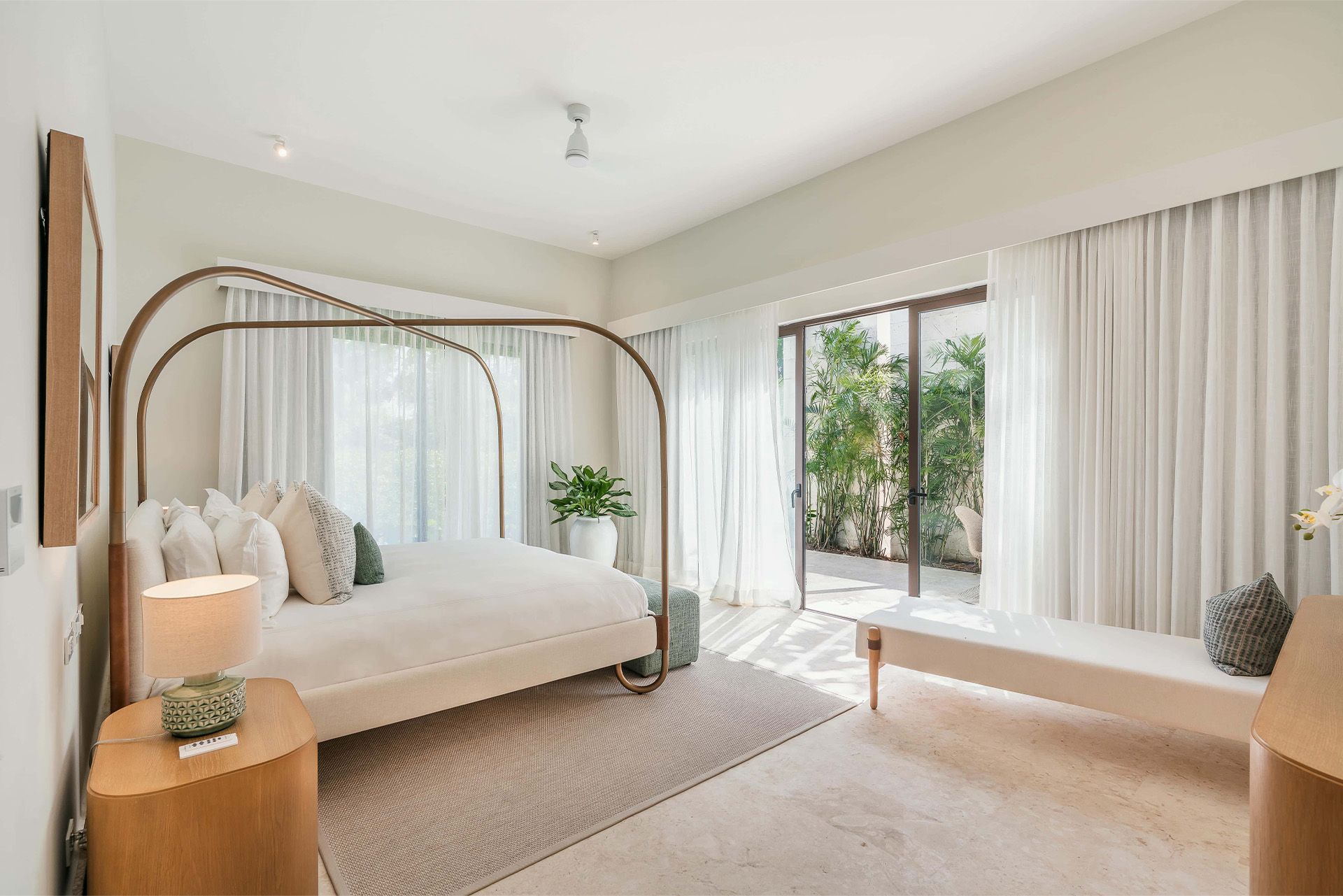 Bright minimalist bedroom with a canopy bed, white curtains, and a sliding glass door to greenery