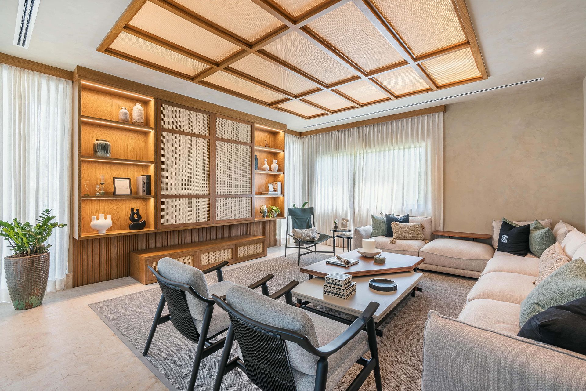 Bright modern living room with beige sectional sofa, wooden shelving, coffee table, and large windows