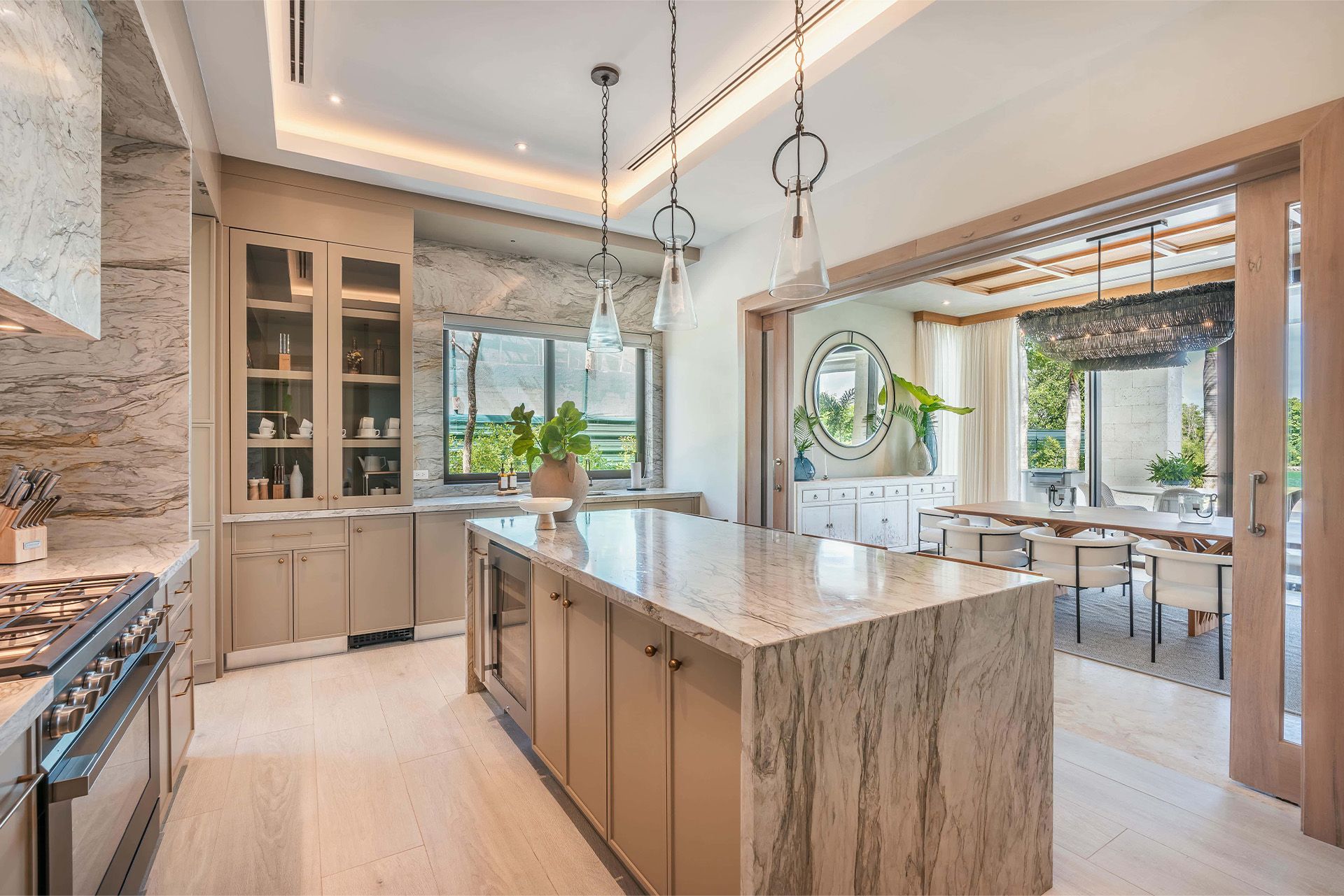 Bright modern kitchen with marble island, pendant lights, and large windows overlooking greenery