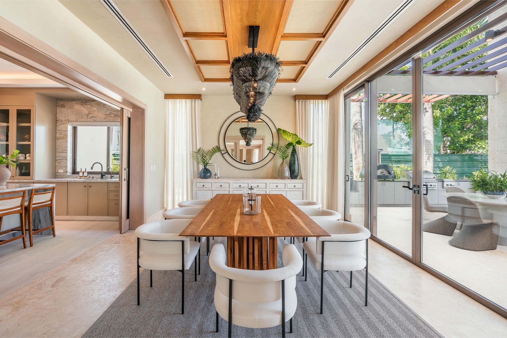 Bright dining room with wood table, white chairs, woven pendant lights, and large glass doors to a patio