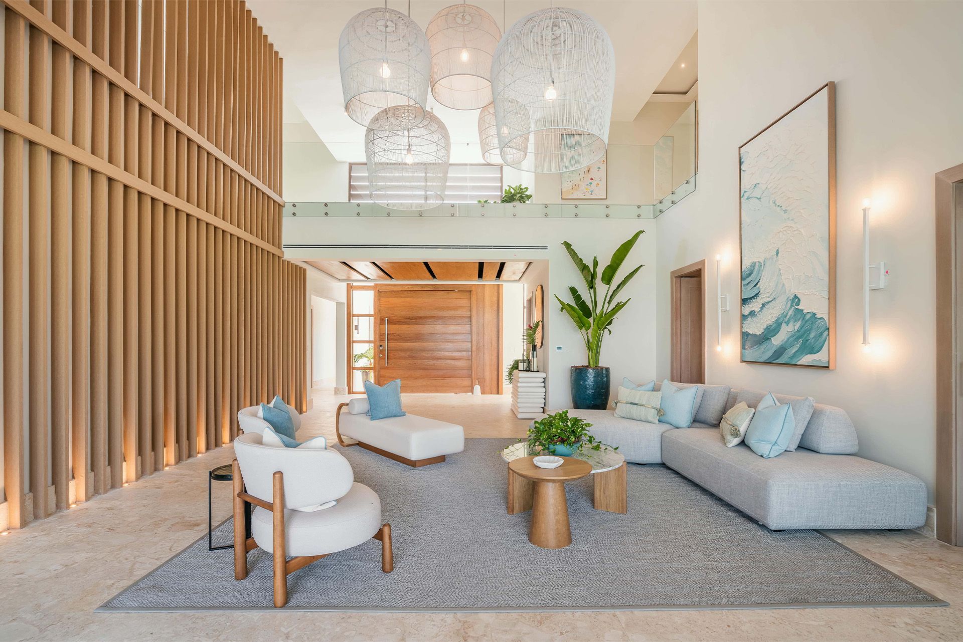 Bright modern living room with gray sofa, white chairs, wood slat wall, large hanging lights, and indoor plants