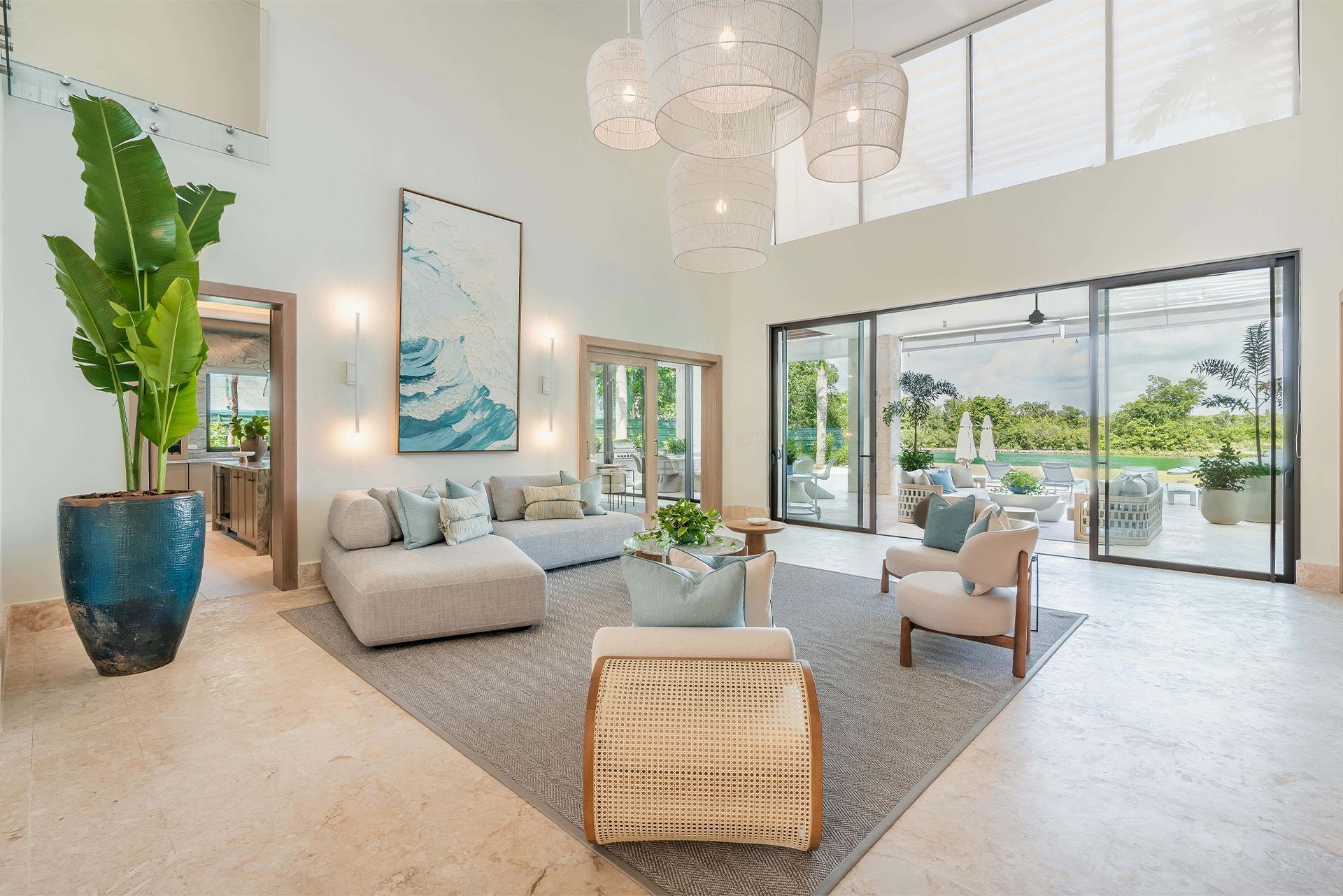 Bright modern living room with large windows, gray sofa, beige chair, blue vase, and a coastal view