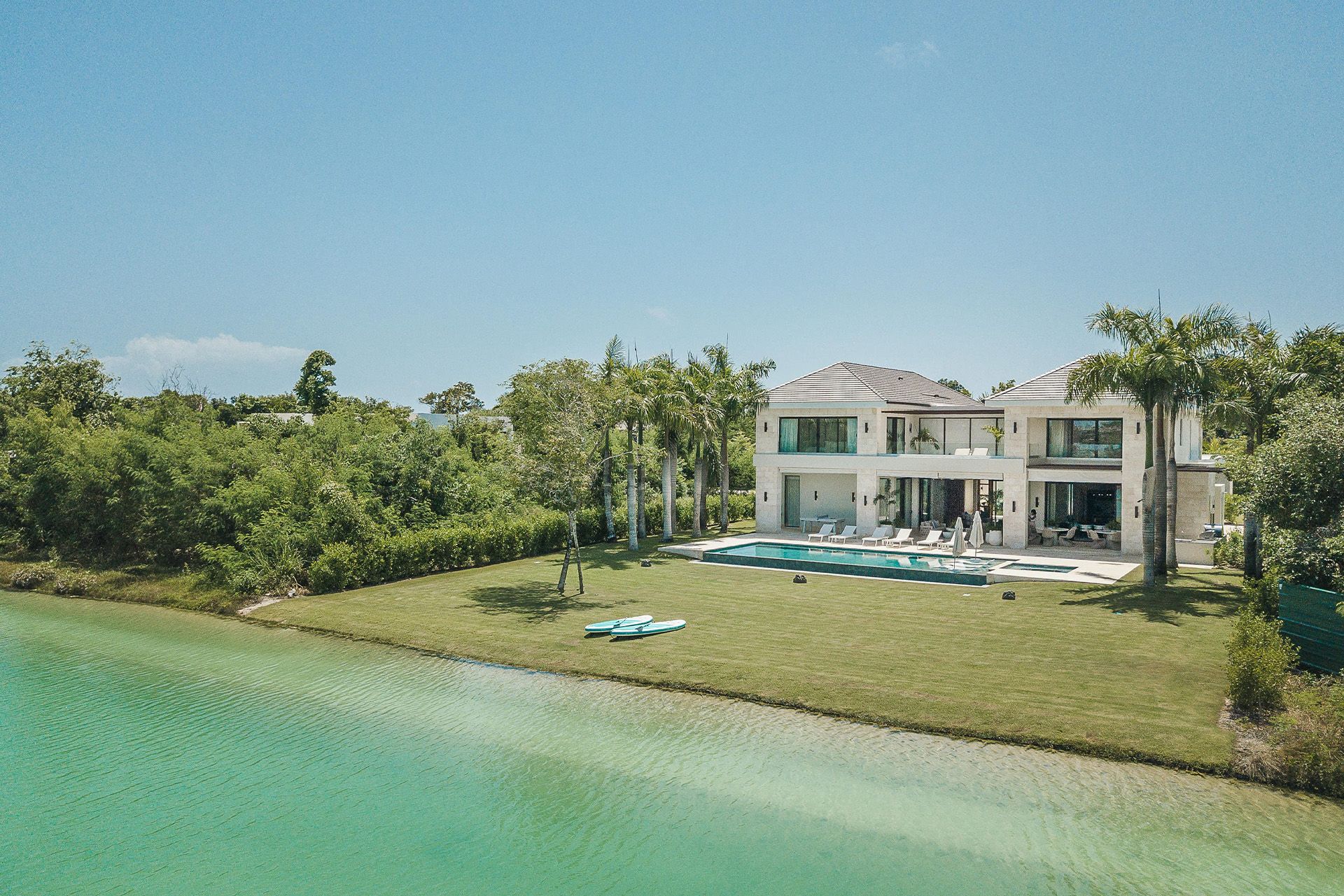 Modern white waterfront villa with pool beside a turquoise lagoon and lush greenery. Mangle 15