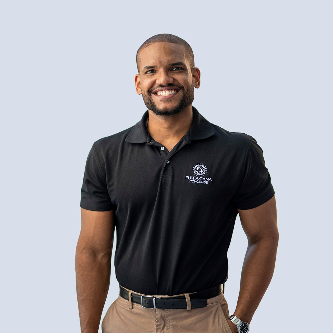 Smiling man in a black polo shirt and khaki pants standing against a light gray background