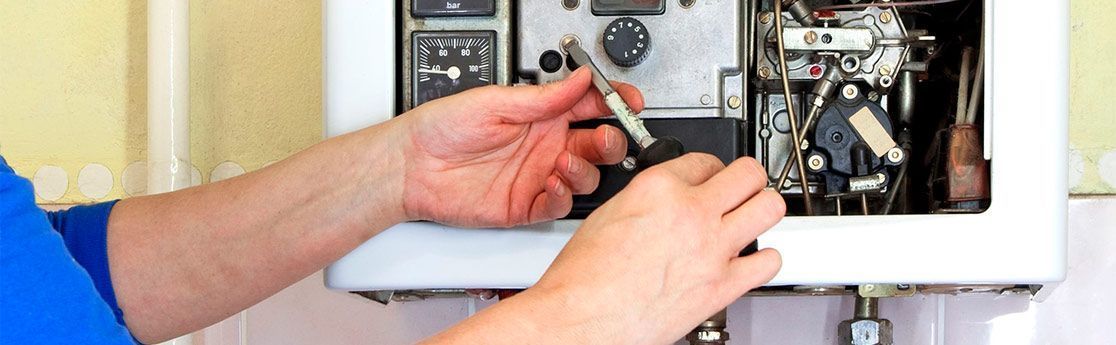 Persona utilizando un destornillador para reparar una caldera mural blanca.
