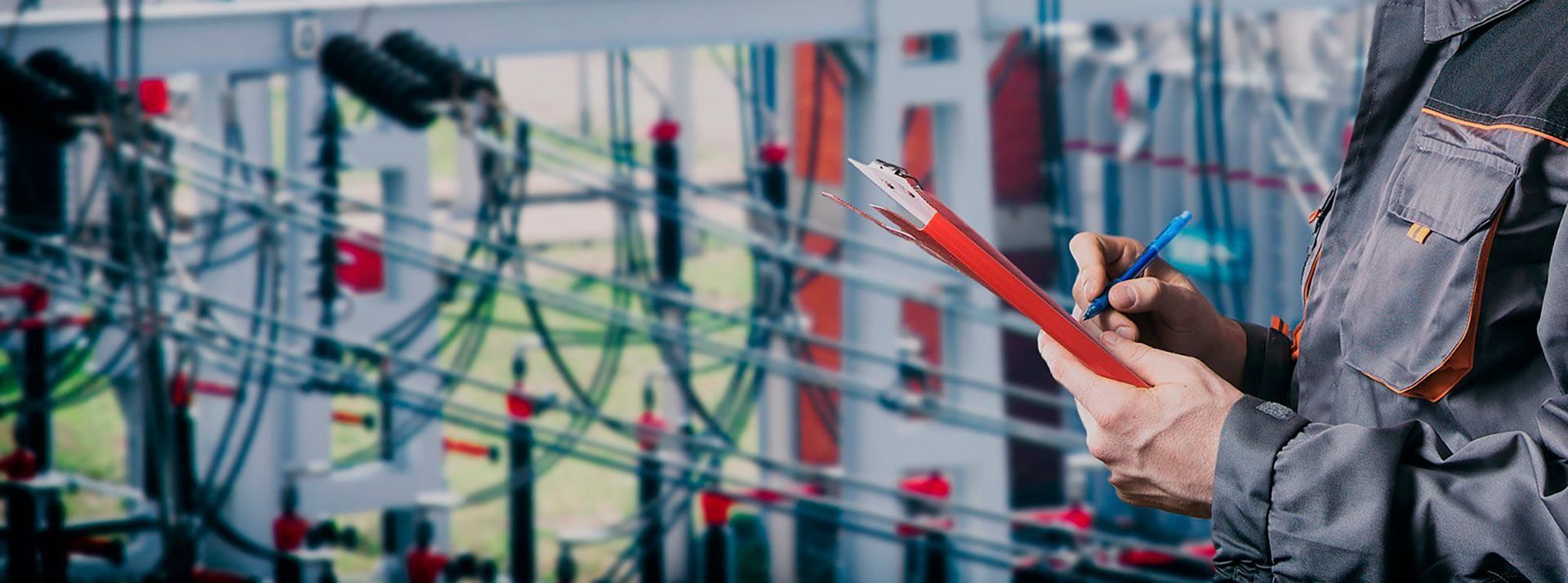 Persona con mono gris, sosteniendo una carpeta y un bolígrafo, inspeccionando maquinaria.