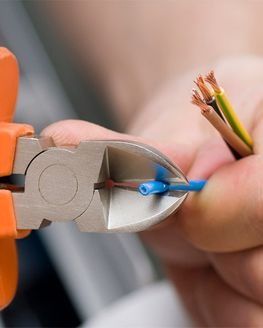 Cortacables cortando cable eléctrico azul; se ven cables marrones, verdes y amarillos.