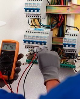 Electricista probando un interruptor automático con un multímetro, que muestra una lectura de 218 voltios.