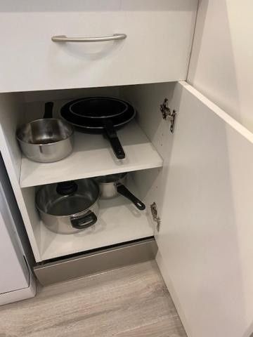 Armario abierto con ollas y sartenes apiladas en estantes blancos.