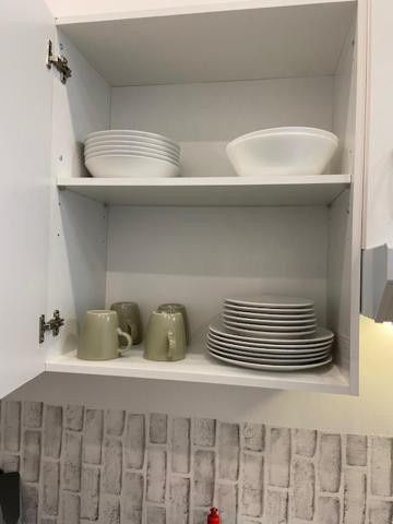 Armario de cocina abierto con platos blancos apilados, cuencos y tazas verdes sobre un salpicadero de azulejos.