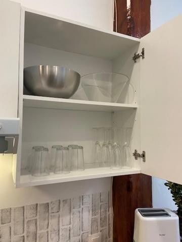 Armario de cocina abierto con cuencos, vasos y una botella apilados en estantes blancos.