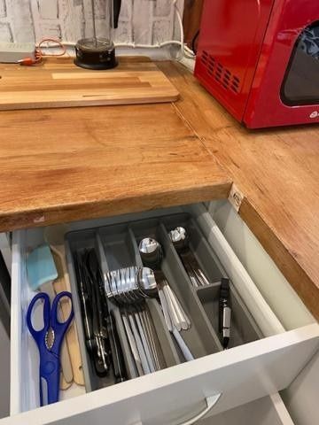 Cajón de cocina con utensilios y tijeras debajo de una encimera de madera junto a un electrodoméstico rojo.