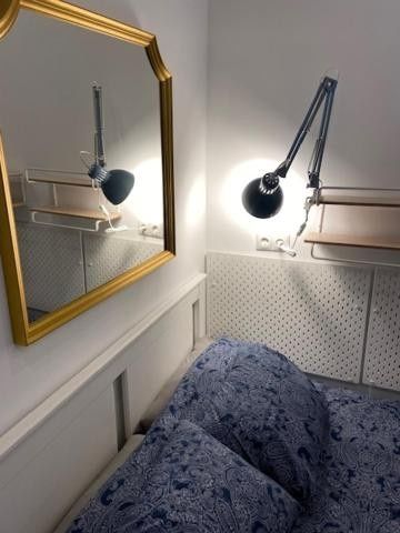Acogedor rincón de dormitorio con espejo con marco dorado, lámpara de pared y ropa de cama con estampado azul.