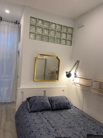 Habitación pequeña con cama, lámpara de pared, espejo y detalles de ventanas de bloques de vidrio.