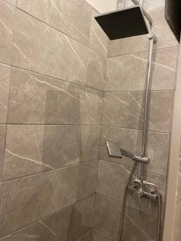 Ducha de baño con paredes de azulejos grises, cabezal de ducha cuadrado negro y grifo cromado.