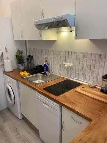 Cocina pequeña con encimeras de madera, armarios blancos, fregadero, fogones, lavavajillas y lavadora.