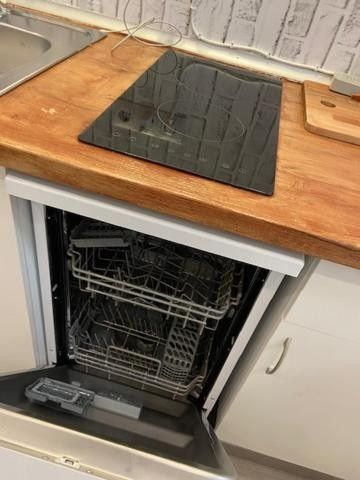 Lavavajillas abierto debajo de una encimera de madera con una alfombrilla de fregadero encima en una cocina.