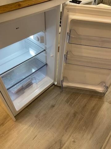 Refrigerador abierto con estantes y compartimentos de la puerta vacíos, sobre un piso de madera en una cocina.