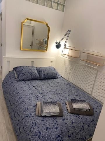Habitación pequeña con una colcha azul, espejo de pared y lámpara regulable junto a estantes de pared.