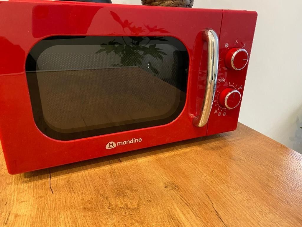 Microondas rojo de encimera con asa cromada sobre una mesa de madera.