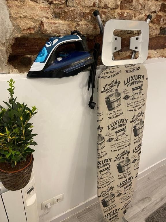 Plancha azul y negra sobre una superficie blanca junto a una funda de tabla de planchar colgante