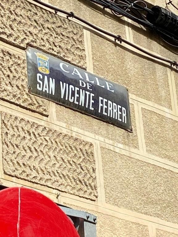 Letrero con la inscripción “San Vicente Ferrer” en la pared de un edificio de color beige con un borde de toldo rojo.