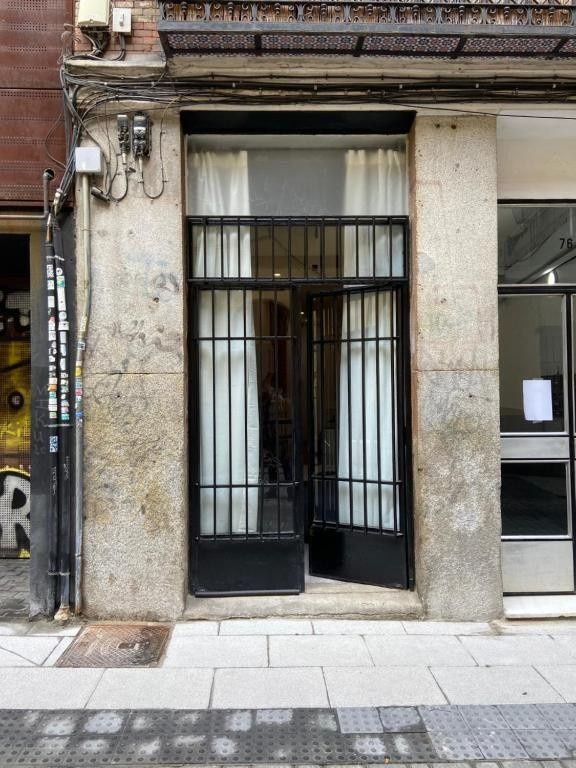 Entrada estrecha a un local comercial con verja de metal negro y cortinas blancas en una fachada de piedra desgastada.