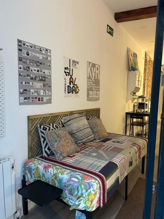 Habitación estrecha con una cama estampada, cuadros en la pared y un pasillo que conduce a una pequeña mesa y una silla.