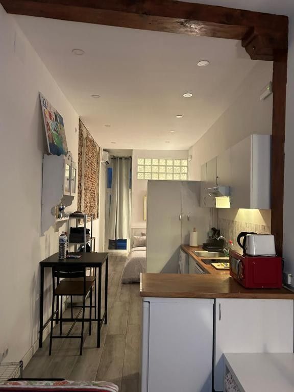 Cocina estrecha de color blanco con encimeras de madera, mesa de comedor negra y lámparas colgantes.