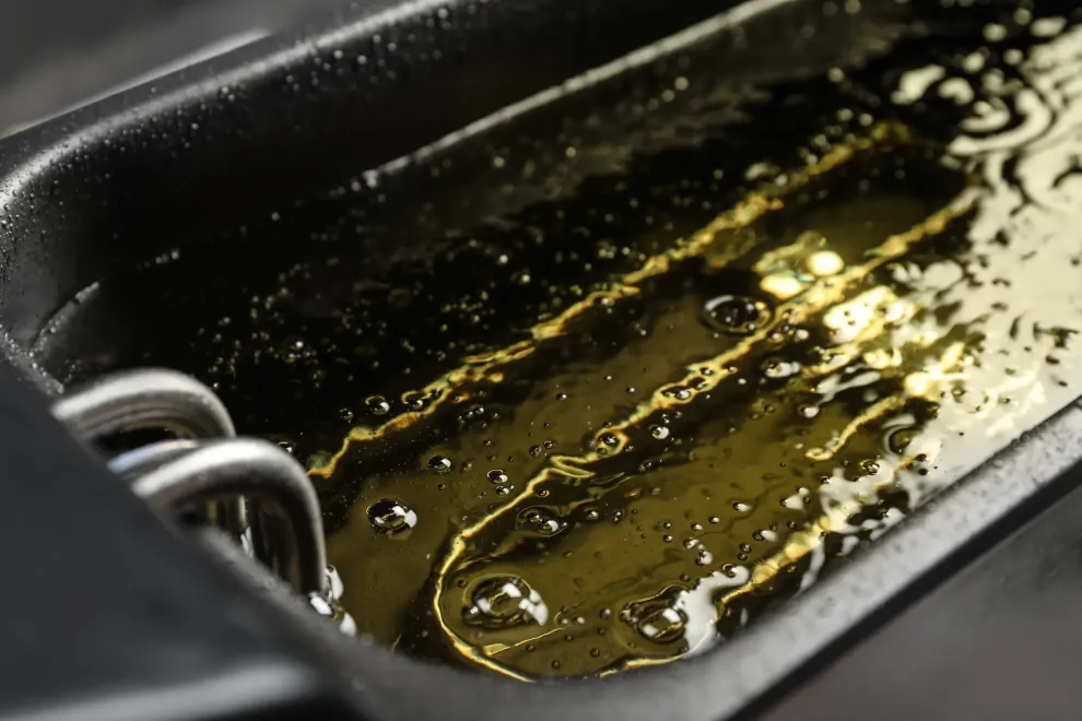 Primer plano del aceite de freír en una sartén negra con un asa de cesta metálica visible.