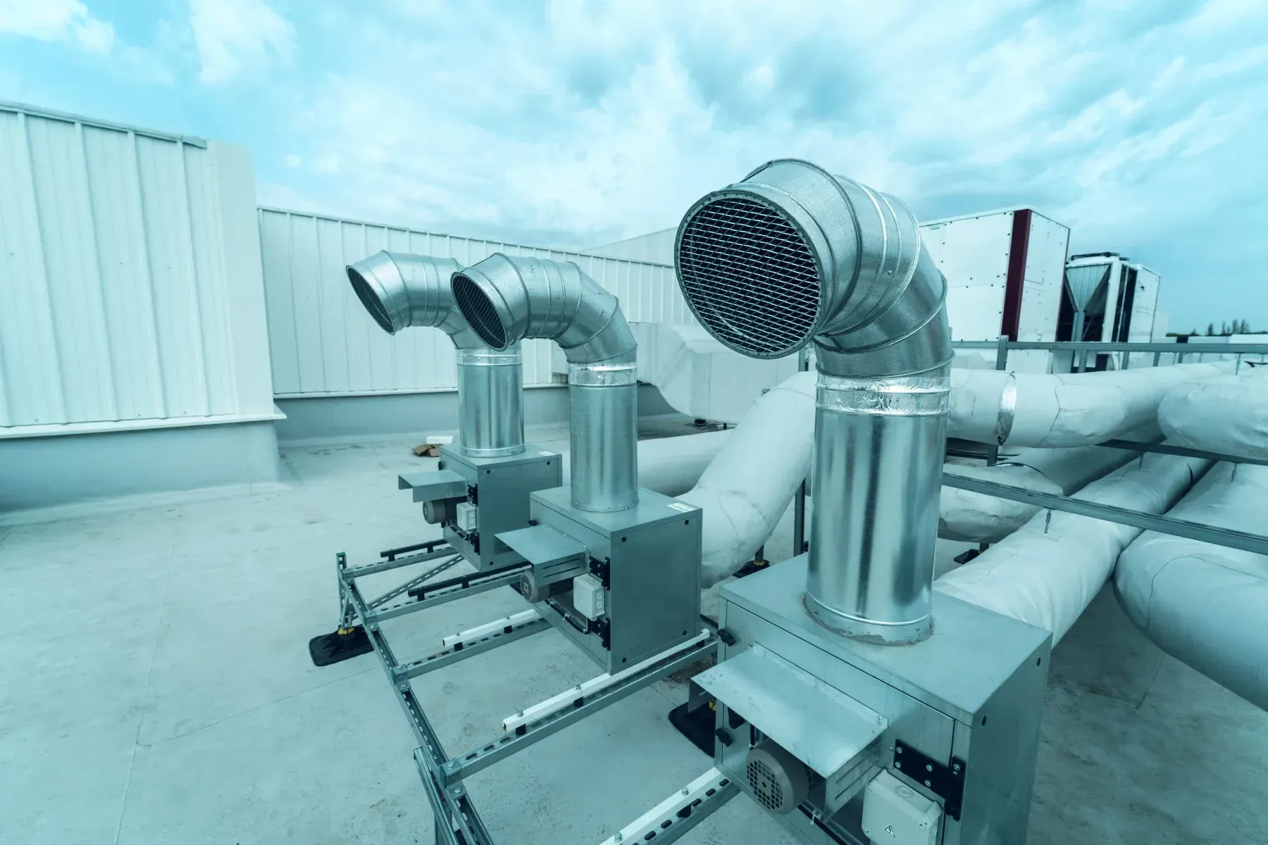 Conductos y ventiladores de climatización industrial instalados en la azotea de un edificio blanco.