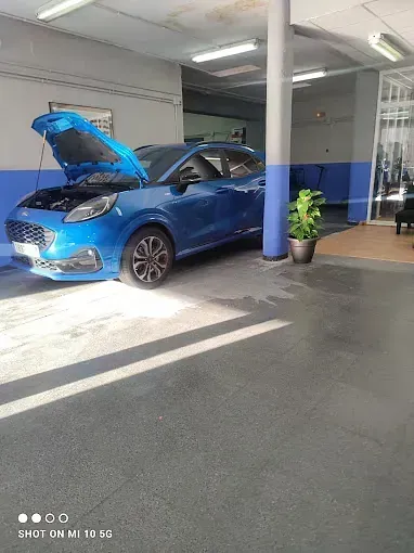 Un coche azul está aparcado en un garaje con el capó levantado.