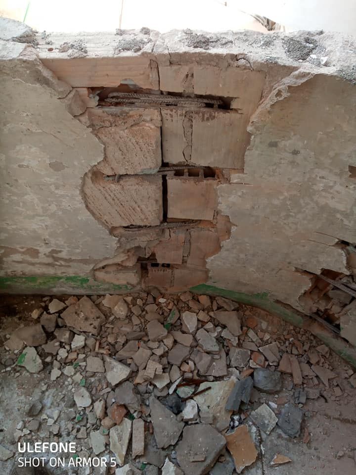 Una pared de ladrillos con un agujero y muchas rocas en el suelo.