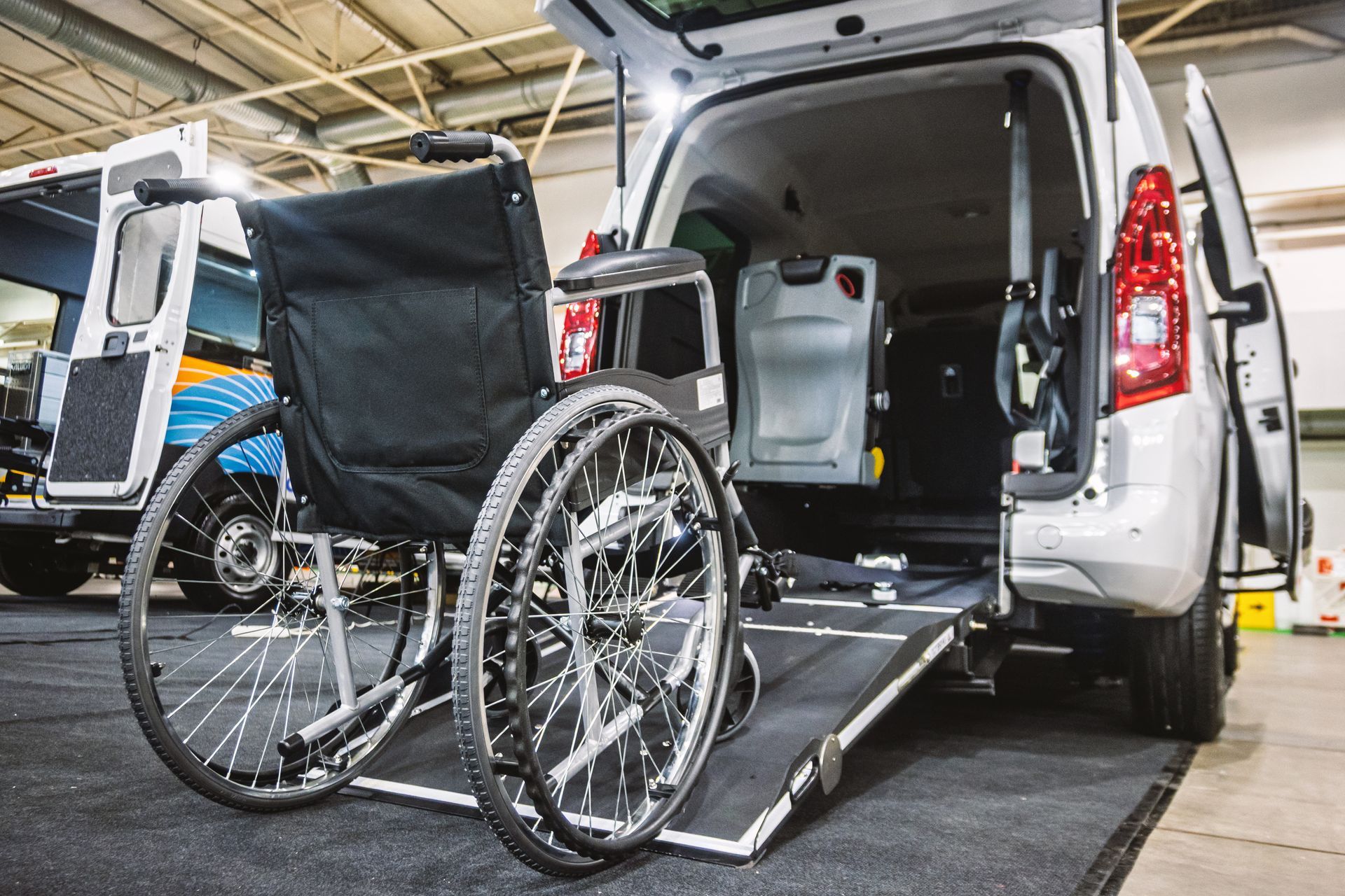 Un fauteuil roulant est chargé dans une ambulance blanche par une rampe arrière, avec un élévateur pour fauteuil roulant en arrière-plan.
