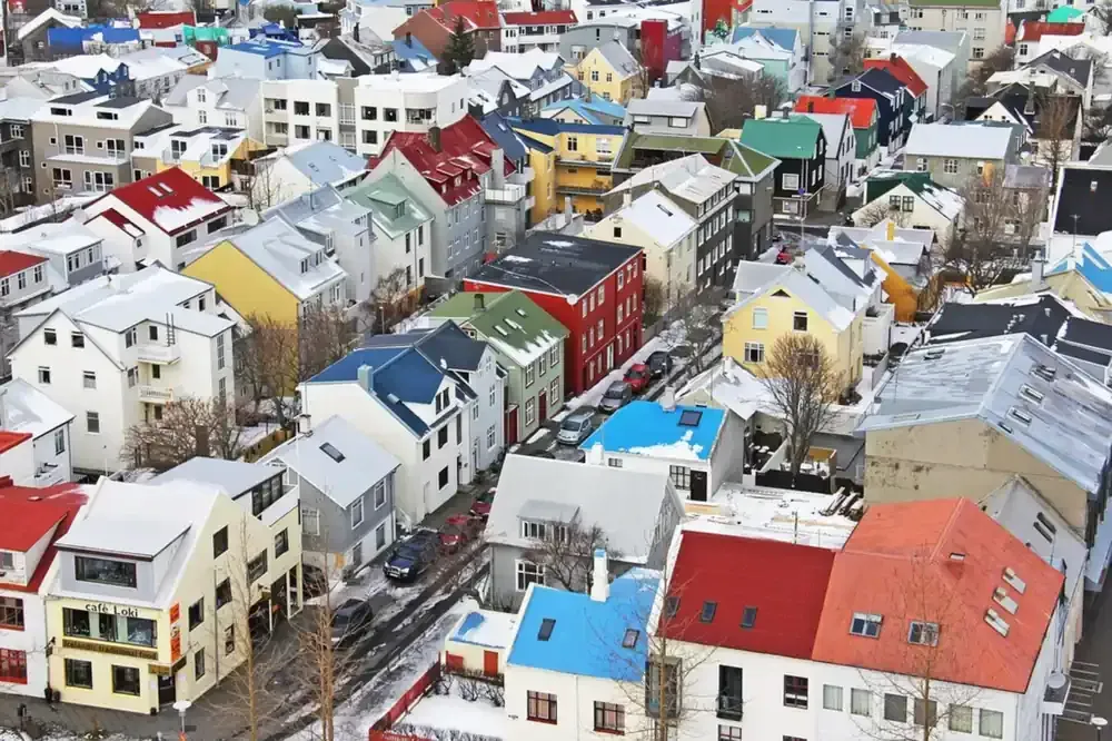 Casas coloridas con techos cubiertos de nieve en una zona urbana densamente poblada, posiblemente Reykjavik.