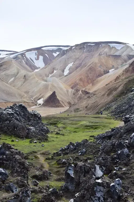 Primer plano rocoso, valle verde y montañas coloridas con manchas de nieve.