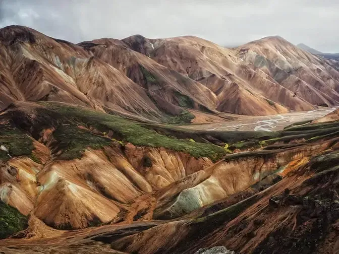 Paisaje montañoso colorido con tonos marrones, amarillos y verdes, terreno erosionado.