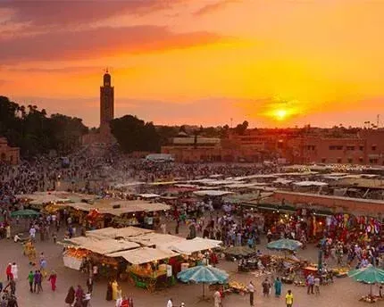 Atardecer sobre la concurrida plaza Djemaa el-Fna, Marrakech. Puestos de mercado, gente y un alto minarete.