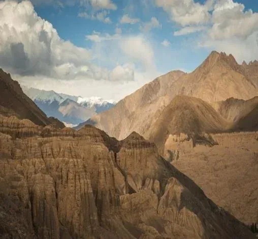Montañas y cañones bajo un cielo azul con nubes esponjosas.