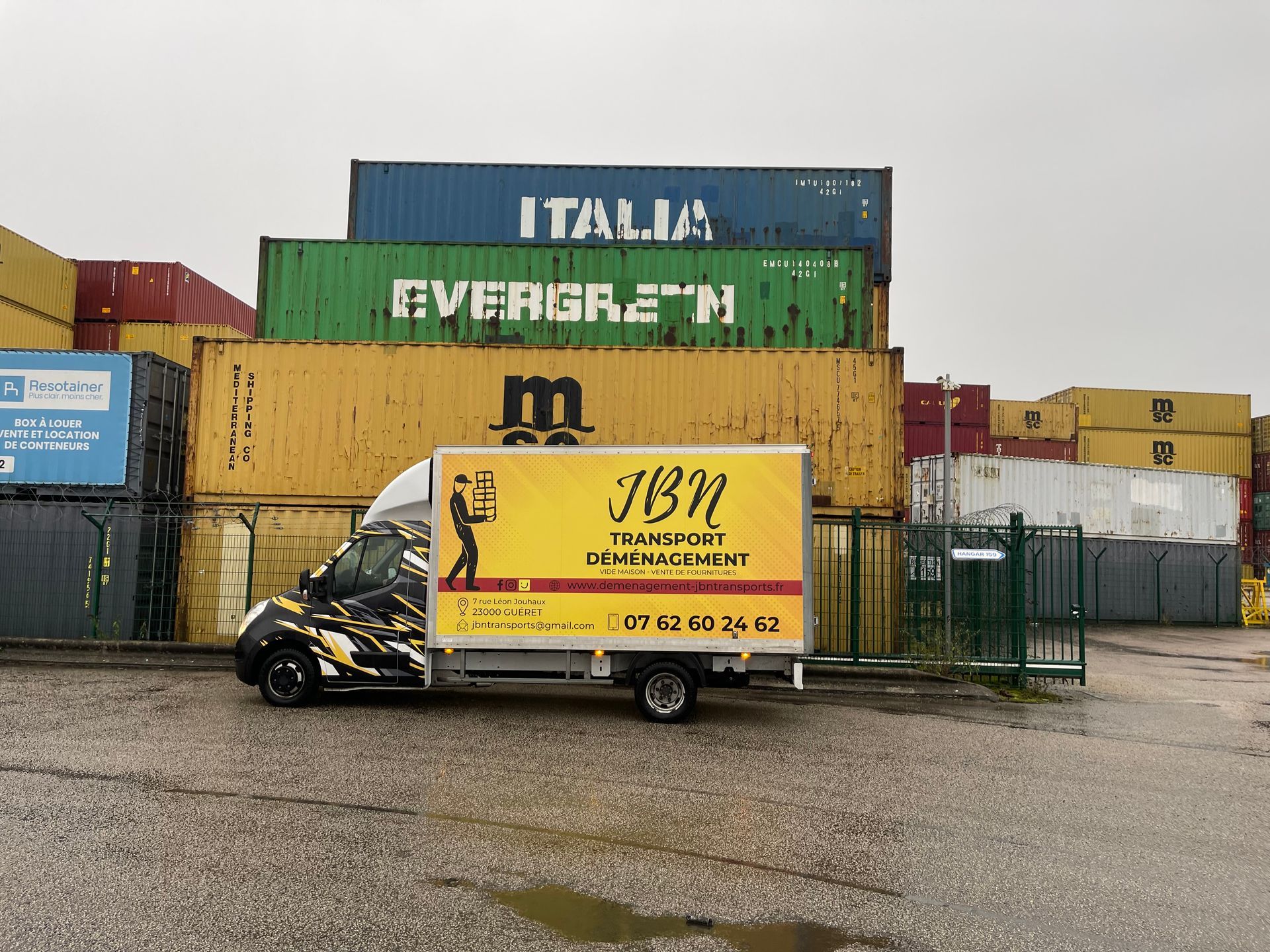 Camion floqué JBN Transport garé devant de grands conteneurs de transport maritime