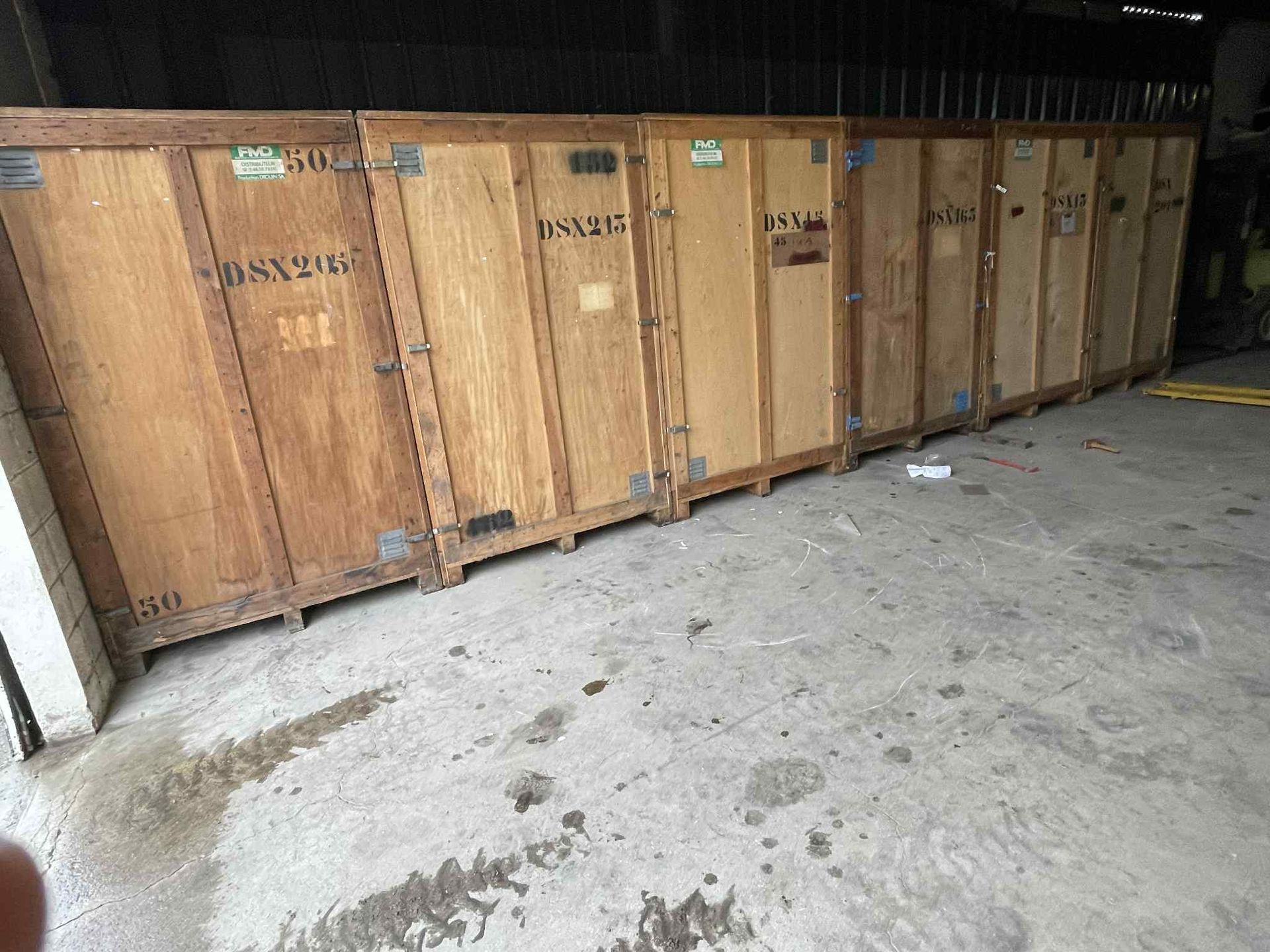 Plusieurs grandes caisses en bois alignées sur un sol en béton, probablement dans un entrepôt.