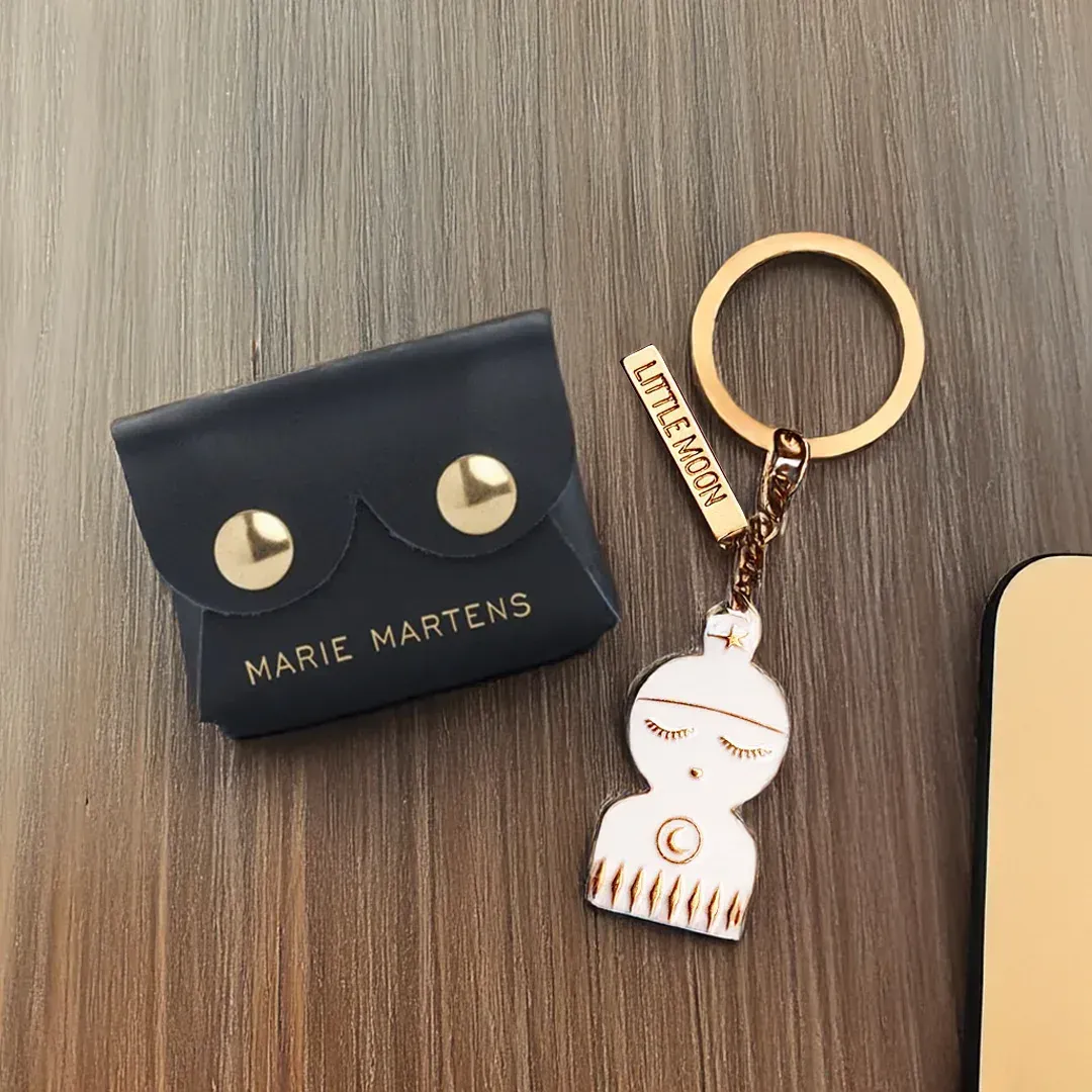 Porte-monnaie Marie Martens bleu foncé et porte-clés doré avec un pendentif poupée.