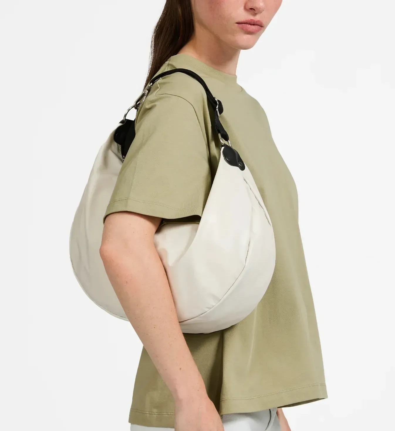 Femme portant une chemise vert clair, avec un grand sac à main blanc en forme de croissant sur l'épaule.