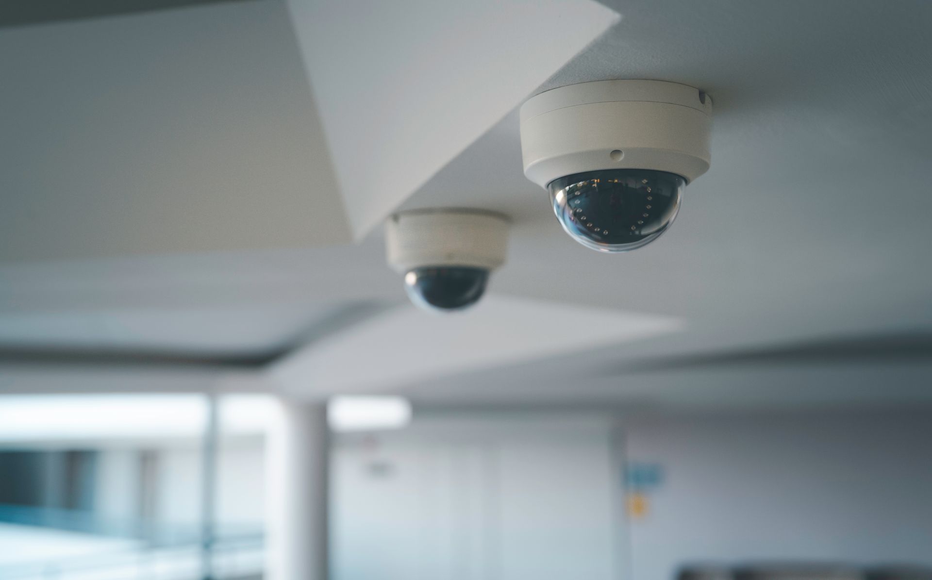 Deux caméras de surveillance en forme de dôme, fixées sur un plafond moderne et orientées de manière à surveiller un espace intérieur.
