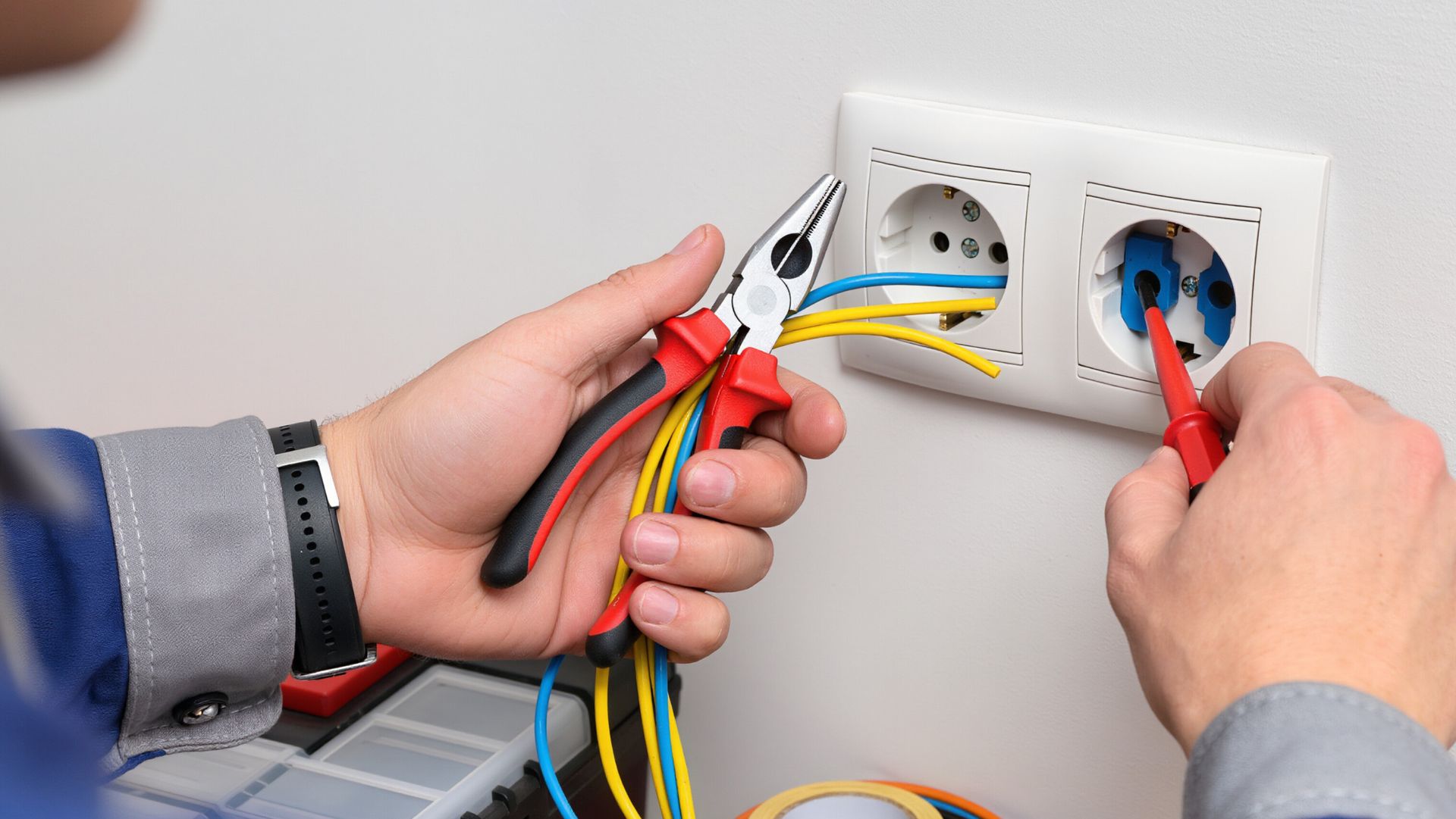 Un électricien, tenant une pince, teste une prise murale dont les fils sont dénudés.